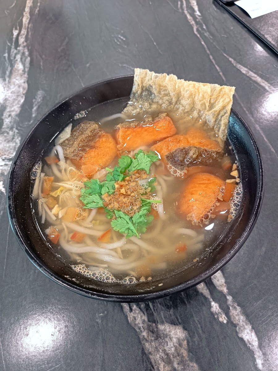 overhead shot of clear fish noodle soup with fried fish and bean curd skin